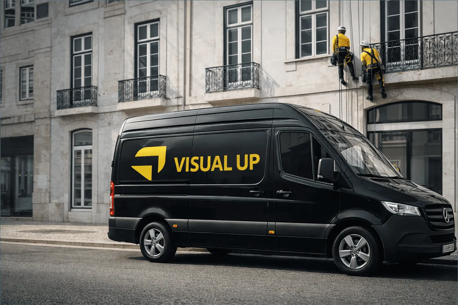 Carrinha preta da Visual Up com a marca em âmbar, estacionada em Lisboa, com dois técnicos suspensos em cordas a trabalhar na fachada.